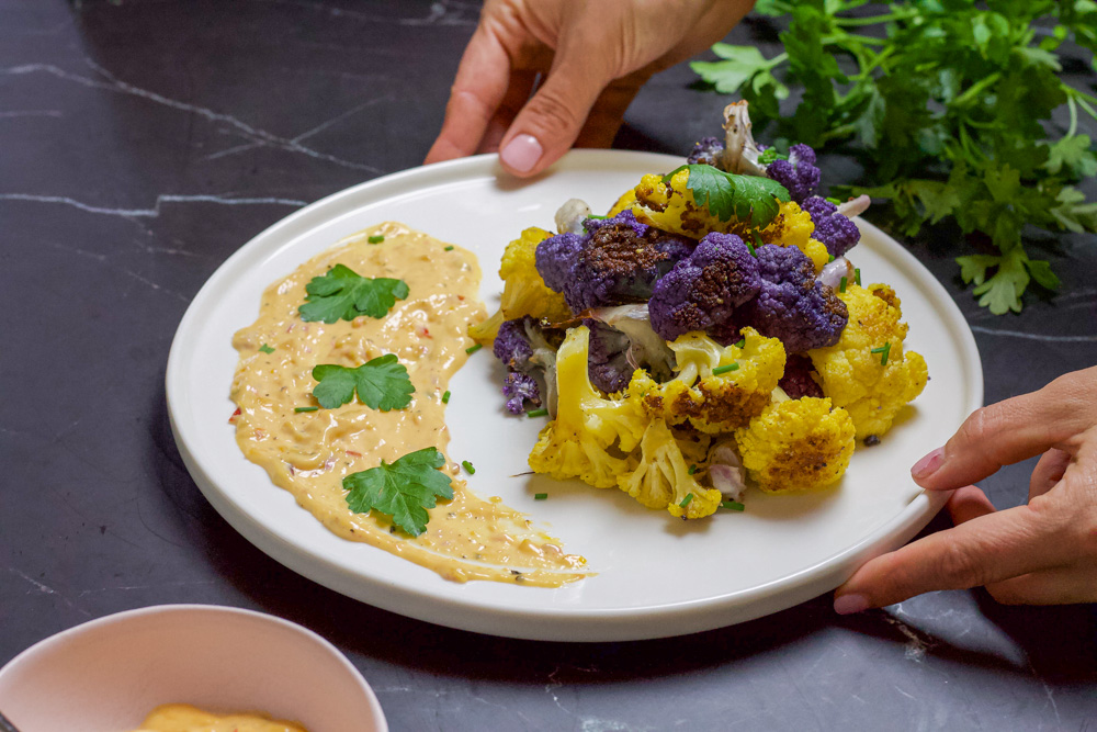 hands serving crispy cauliflower with Calabrian chili mayo and parsley