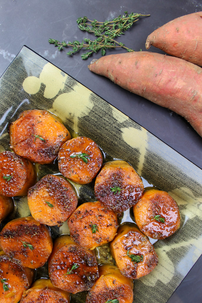 brown sugar spiced sweet potatoes on a black and gold plate with thyme