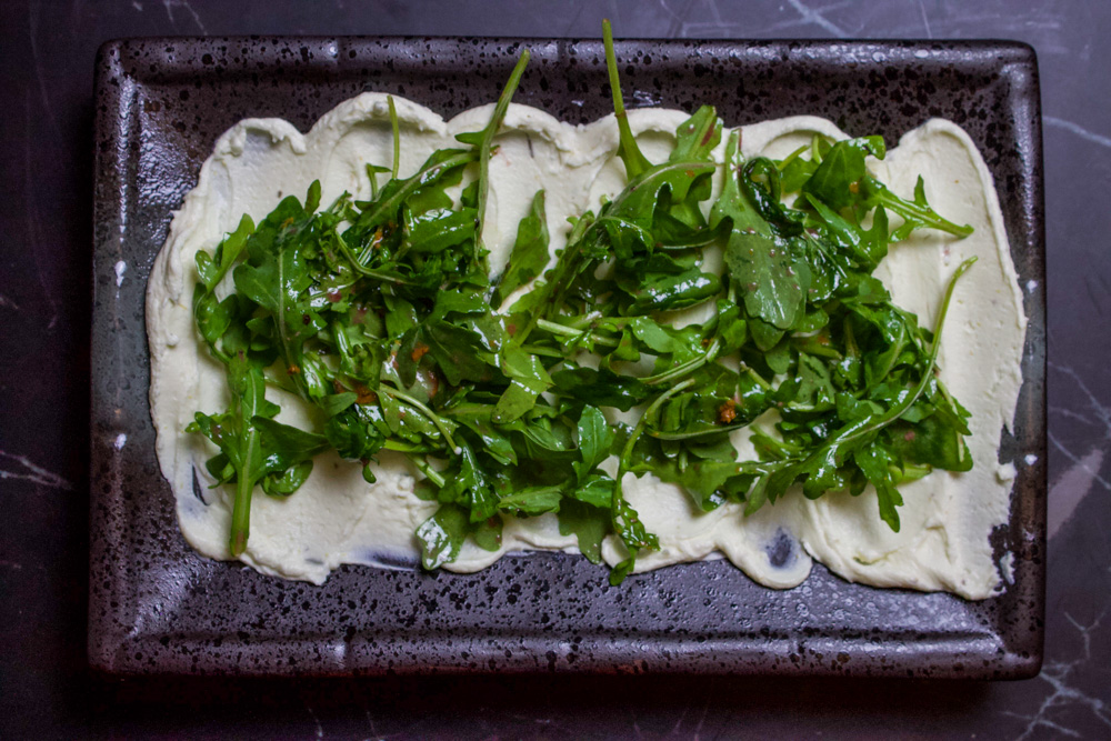 whipped goat cheese on black plate with arugula