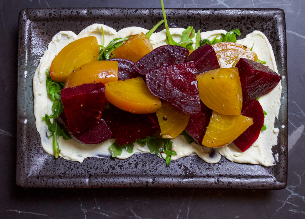 whipped goat cheese on black plate with arugula and beets