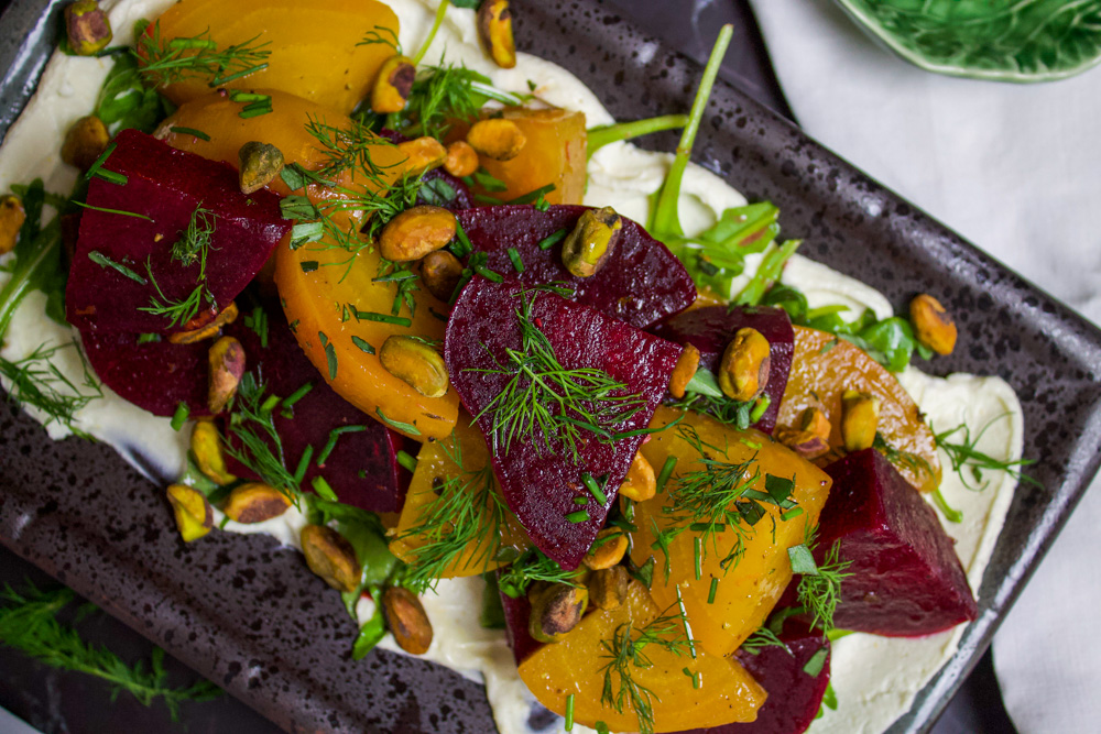 beet salad on a bed of whipped goat cheese topped with herbs and pistachios