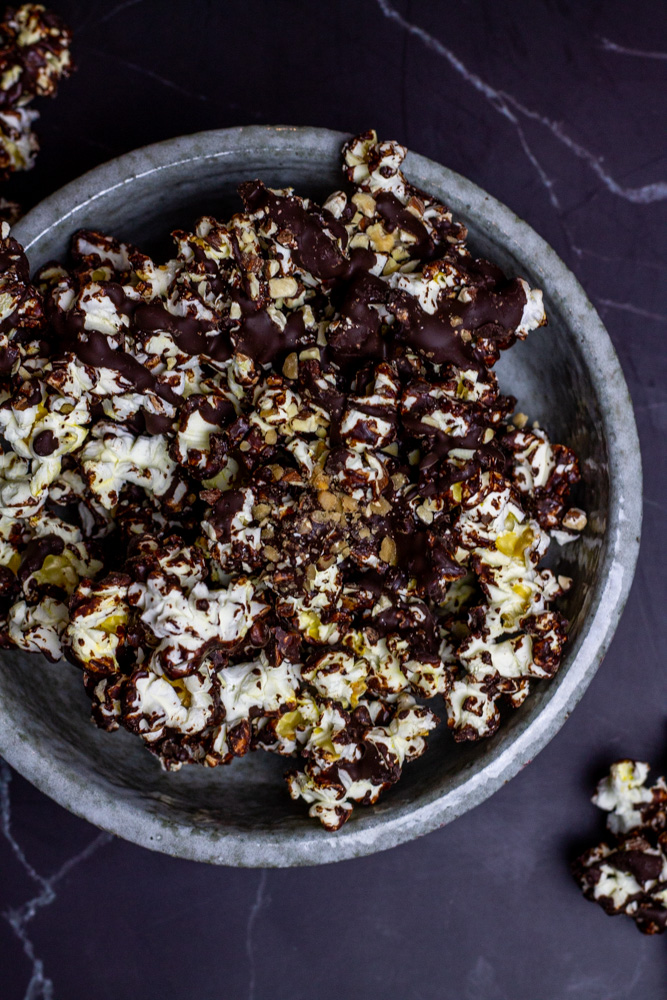 chocolate toffee popcorn with almonds in grey bowl on black marble counter