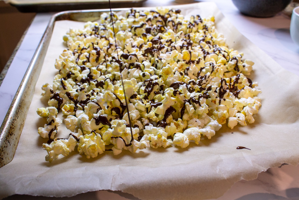 popcorn on parchment lined tray drizzling chocolate