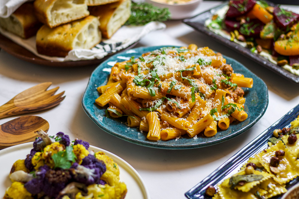 spicy sausage rigatoni topped with basil and parmesan surrounded by bread, beets, and cauliflower