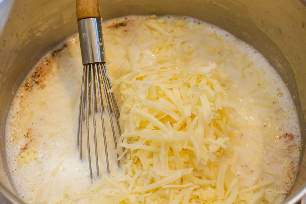 making cheese sauce for mac and cheese in pot with whisk