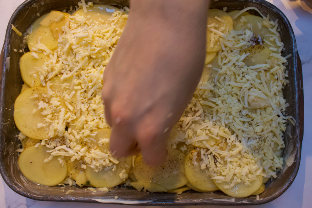 sprinkling cheese on potatoes in a baking dish