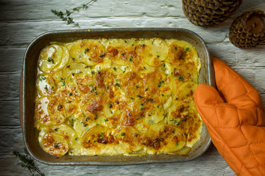 scalloped potatoes in a baking dish topped with thyme held by orange mit